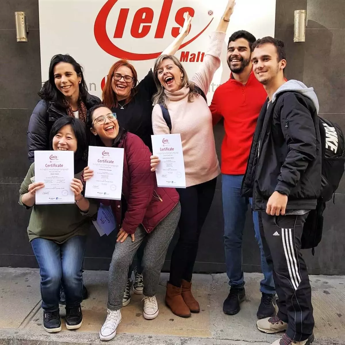 Grupo de 6 estudantes com seus diplomas em frente à entrada da IELS Malta