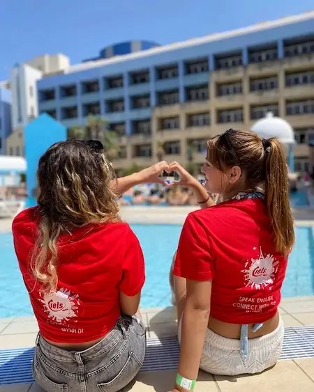 Two IELS supervisors in front of a pool making a heart with their hands