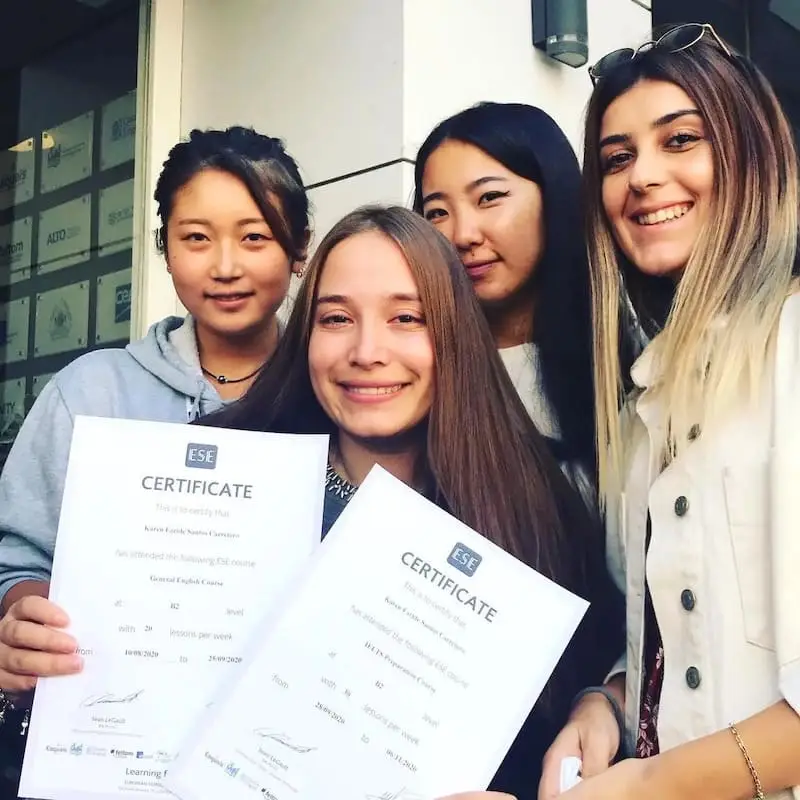Cuatro estudiantes sonrientes con sus diplomas de inglés