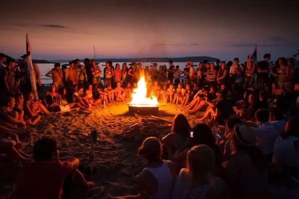 Group of young people on a language stay in Malta gathered around a campfire on the beach at sunset