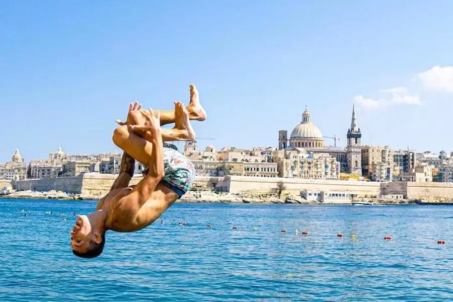 Giovane che esegue un salto in mare con vista su La Valletta