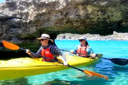 Two women in a kayak passing under an arch in Malta